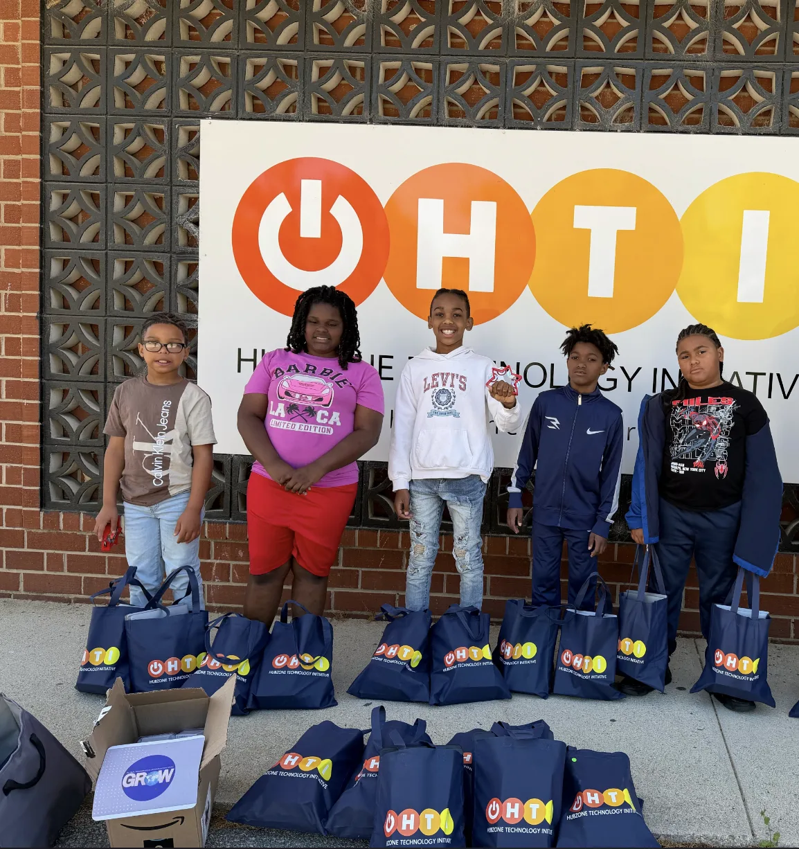 Young HTI GROW participants standing with HUBZone Technology Initiative laptop bags.